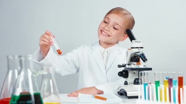 Joven estudiante de química sosteniendo tubo de ensayo con productos químicos rojos y mirando a la cámara con sonrisa — Vídeos de Stock