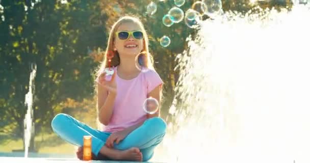 L'enfant de la fontaine est émotionnel. Fille soufflant bulles de savon près de la fontaine — Video