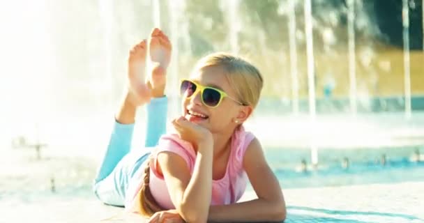 Portrait child lying on fountain background at sunny day and waving hand — Stock Video