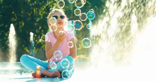 Mooi shot van meisje blazen van zeepbellen in de buurt van fontein en lachen — Stockvideo