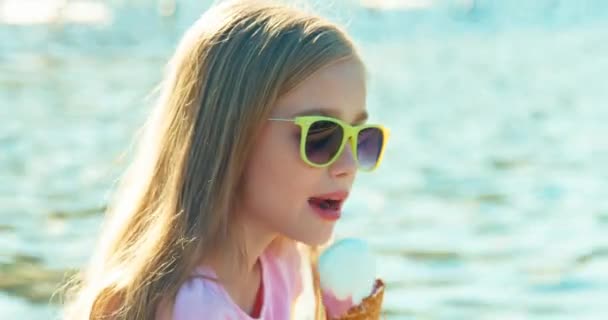 Närbild porträtt lyckligt barn flicka 7-8 år äter glass sitter nära fontänen och ler mot kameran. Mot solen — Stockvideo