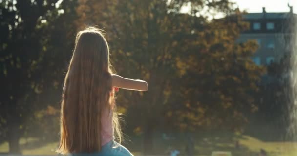 Menina feliz sentado perto da fonte e soprando bolhas de sabão — Vídeo de Stock