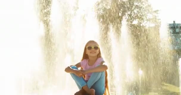 Kind Mädchen 7-8 Jahre entspannen in der Nähe von Brunnen Hintergrund bei sonnigem Tag und Blick in die Kamera — Stockvideo