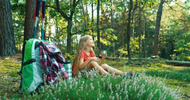Caminhante menina criança 8-9 anos relaxante e beber chá na floresta e sorrindo para a câmera — Vídeo de Stock