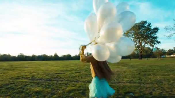 Kind die dwars over het veld bij zon in zonsondergang en houdt haar witte ballonnen — Stockvideo