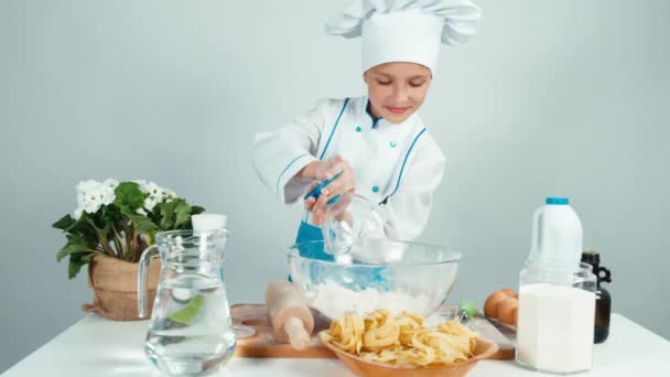 Fiatal baker pour lisztet a tálba a konyhaasztalnál, és mosolyogva kamera — Stock videók