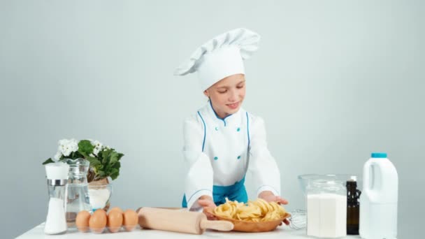 Ritratto cuoco carino cuoco ragazza tiene piatto con spaghetti e te lo dà a macchina fotografica. Bambino in piedi in cucina sorridente isolato su bianco — Video Stock