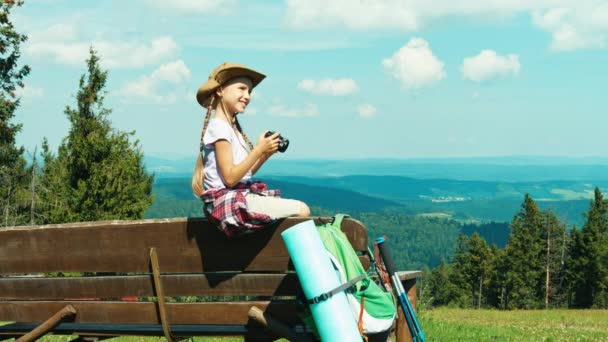 Küçük uzun yürüyüşe çıkan kimse kız 7-8 yaş arası dağlar arka plan üzerinde bankta oturmuş ve fotoğrafları yapma — Stok video