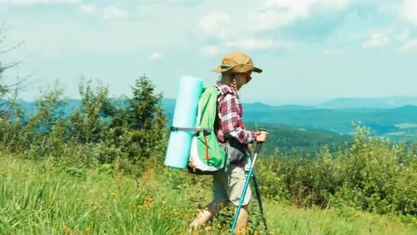 Pequeña chica excursionista va doun la colina en las montañas de fondo y sonriendo a la cámara — Vídeos de Stock