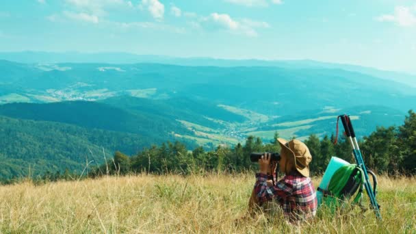 Portrét malý turista dítě dívka 7-8 let pomocí dalekohledu a sedí na trávě na pozadí hory — Stock video