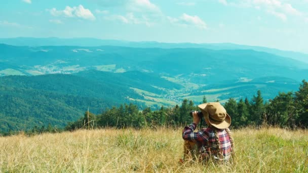 Porträtt lite hiker barn flicka 7-8 år tittar på avstånd genom kikare och sitter på gräset på bergen bakgrund — Stockvideo