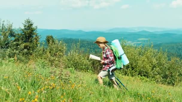 Lilla hiker flicka tittar på karta och går upp till kullen på bergen bakgrund och leende på kamera — Stockvideo