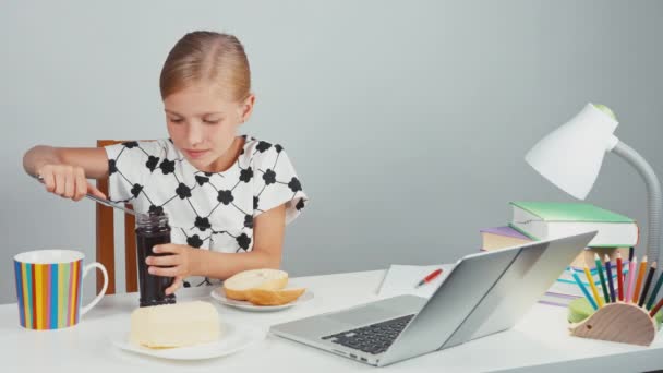 Портретна школярка 7-8 років за допомогою ножа робить бутерброд з маслом і варенням, сидячи за столом ввечері — стокове відео
