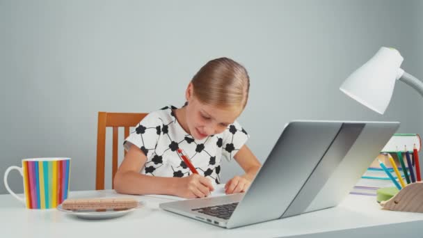 Studentessa mangiare wafer e qualcosa di scrivere nel suo taccuino seduto alla scrivania e sorridente — Video Stock