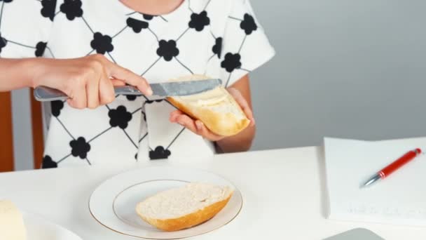 Niña de 7-8 años aplicando mantequilla al pan sentado a la mesa — Vídeos de Stock