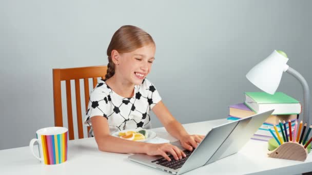 Uczennica, przy użyciu swojego laptopa i zabawy z słodycze siedzi przy biurku w godzinach wieczornych, śmiejąc się z aparatu — Wideo stockowe