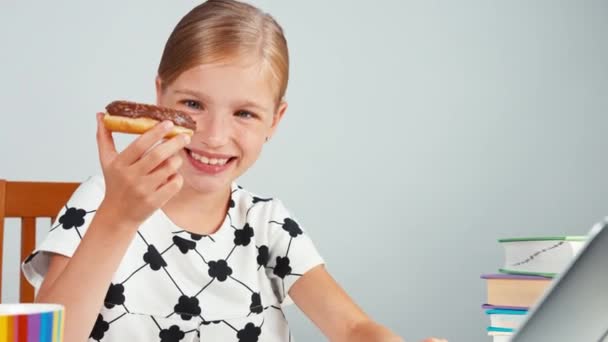 女子高生ドーナツを食べると、夕方には、机に座って彼女のラップトップを使用しています。パン — ストック動画