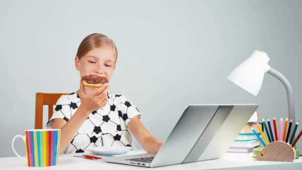 Schoolmeisje donut eten en met behulp van haar laptop zitten aan de balie in de avond. Duim omhoog. OK — Stockvideo