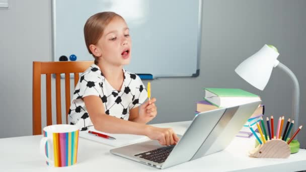 Schoolgirl using her laptop and laughing. Kid licking lollipop and smiling at camera. Child sitting at the desk in the evening — Stock Video