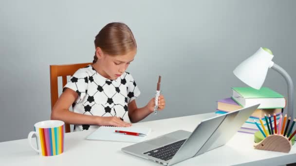 Meisje 7-8 jaar holding een chocolade tegel en de kruimels van de tafel veegt. Kind zit op de tabel en huiswerk Rechtenvrije Stockvideo