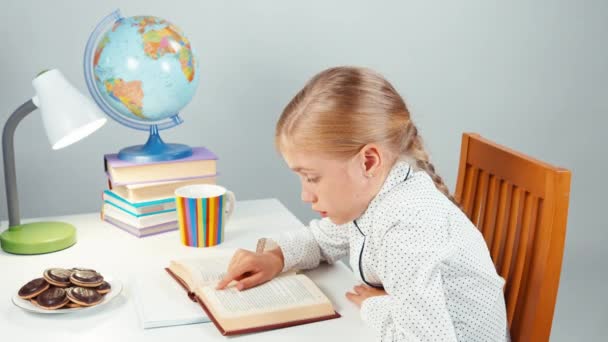 Niña retratista leyendo un libro y riendo. Niño sentado en la mesa aislado en blanco — Vídeo de stock