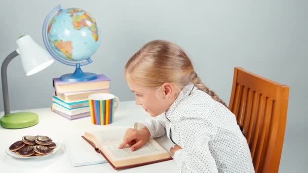 Školačka dítě čte knihu večer a jíst čokoládové cookies — Stock video
