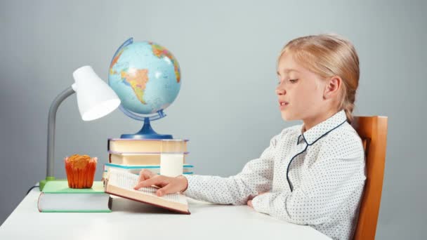 Skolflicka 7-8 år läsa bok konsumtionsmjölk och ler mot kameran isolerad på vit — Stockvideo
