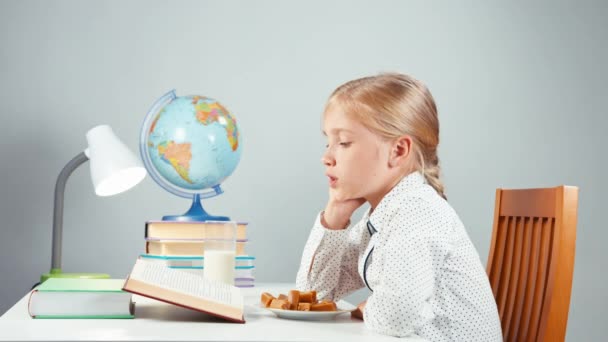 Portret profiel blonde school meisje 7-8 jaar lezen boek en consumptiemelk zitten aan de tafel geïsoleerd op wit in de nacht — Stockvideo