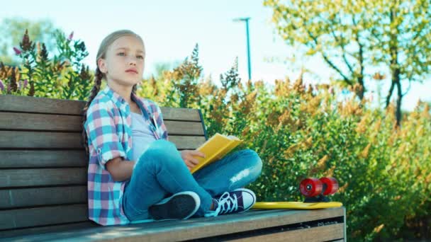 Parádění dívka sedí na lavičce a čtení knihy — Stock video