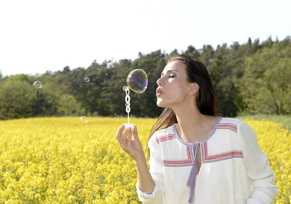 菜の花畑でシャボン玉を吹く若い女性 — ストック写真