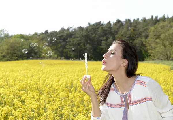 菜の花畑でシャボン玉を吹く若い女性 — ストック写真