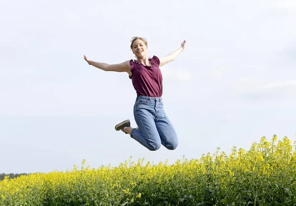 菜の花畑で跳躍うれしそうな若い女性 — ストック写真
