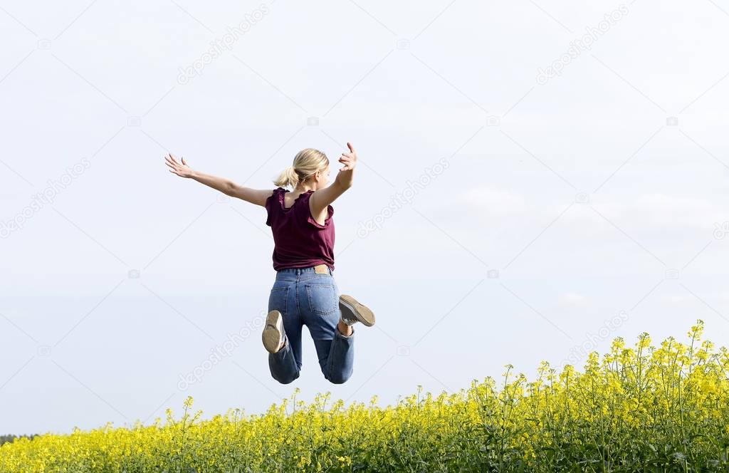 joyful young  woman leaping in the rape field, rear view