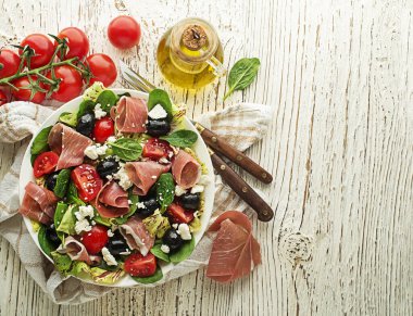 Sağlıklı yeşil salata, prosciutto, zeytin, domates ve ahşap masa arkasında taze peynir. Sağlıklı yemek..