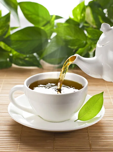 茶壶将新鲜的热茶倒入杯中 背景为花园 茶点休息时间 — 图库照片