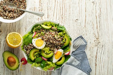 Sağlıklı yeşil salata, kinoa, yumurta ve ahşap arka planda avokado.