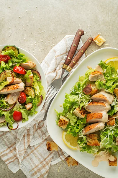Healthy chicken meals with grilled chicken, vegetables, croutons and creamy sauce on grey background. Healthy lunch plates.