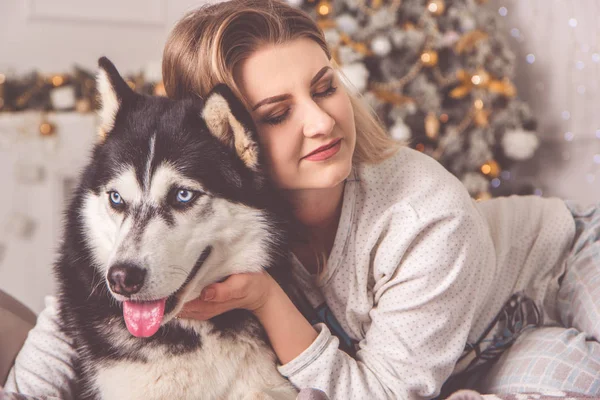 Dziewczyna z psem husky w łóżku obok choinki — Zdjęcie stockowe