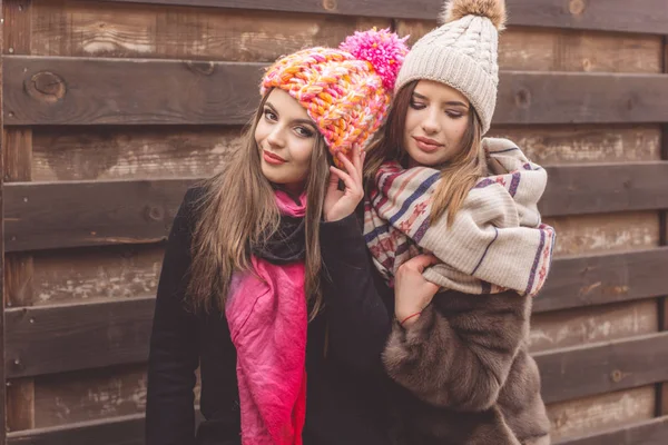 Las niñas están usando ropa de invierno cerca de la pared de madera —  Fotos de Stock
