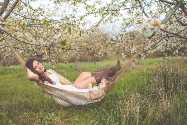 Šťastná dívka s matkou odpočívá v houpací síti venku — Stock fotografie