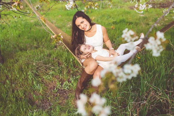 Šťastná dívka s matkou se odpočívá v houpací síti venku — Stock fotografie