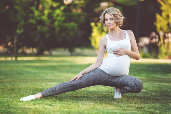 Hermosa mujer embarazada deportiva delgada está haciendo deportes sobre hierba verde —  Fotos de Stock