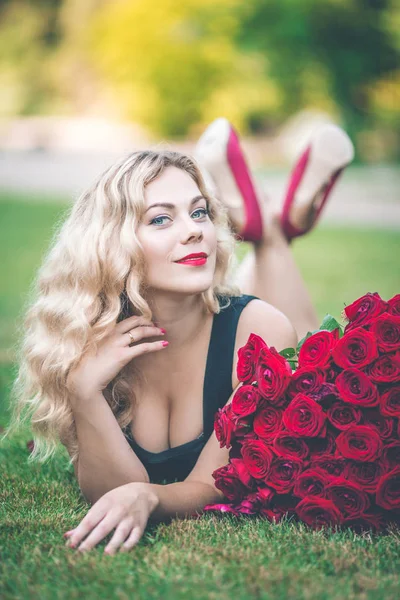 优雅的金发女子躺在绿色的草坪上, 大花束101红玫瑰 — 图库照片