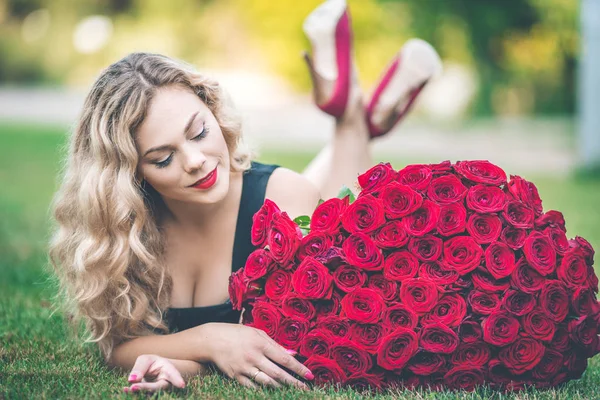 Eleganckie Piękna Blondynka kobieta ma na sobie czarny moda na zielony trawnik z wielki bukiet czerwonych róż 101 — Zdjęcie stockowe
