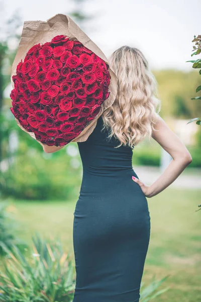 优雅漂亮的女人背观穿着黑色的时尚礼服, 捧着大花束的101朵红玫瑰 — 图库照片