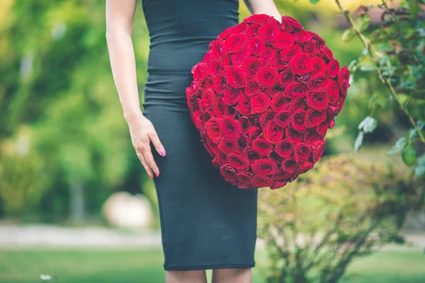 Elegant beautiful woman is wearing black fashion dress is holding big bouquet of 101 red roses — Stock Photo, Image