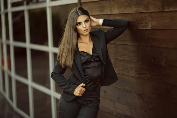 Portré, divat komoly üzleti lány visel fekete hivatalos ruhák nagy üveg ablakok és fából készült fal közelében — Stock Fotó