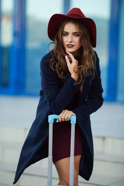 Mooi blij meisje is het dragen van mode kleding en hoed in de buurt van luchthaven met koffer. Foto's concept voor mensen reizen. — Stockfoto