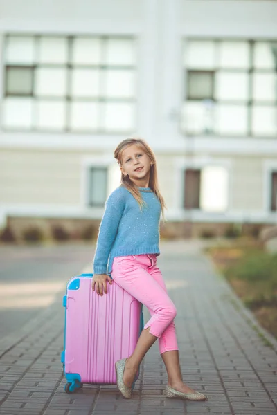 Szczęśliwa dziewczynka siedzi na różowy walizka jest gotowy do podróży — Zdjęcie stockowe
