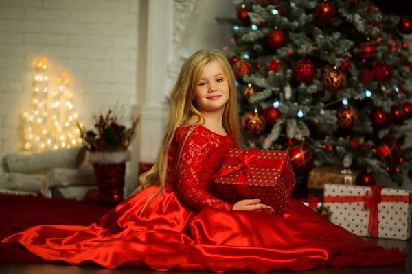 Menina loira bonita está vestindo vestido vermelho moda perto de árvore de xmas decorada e lareira — Fotografia de Stock